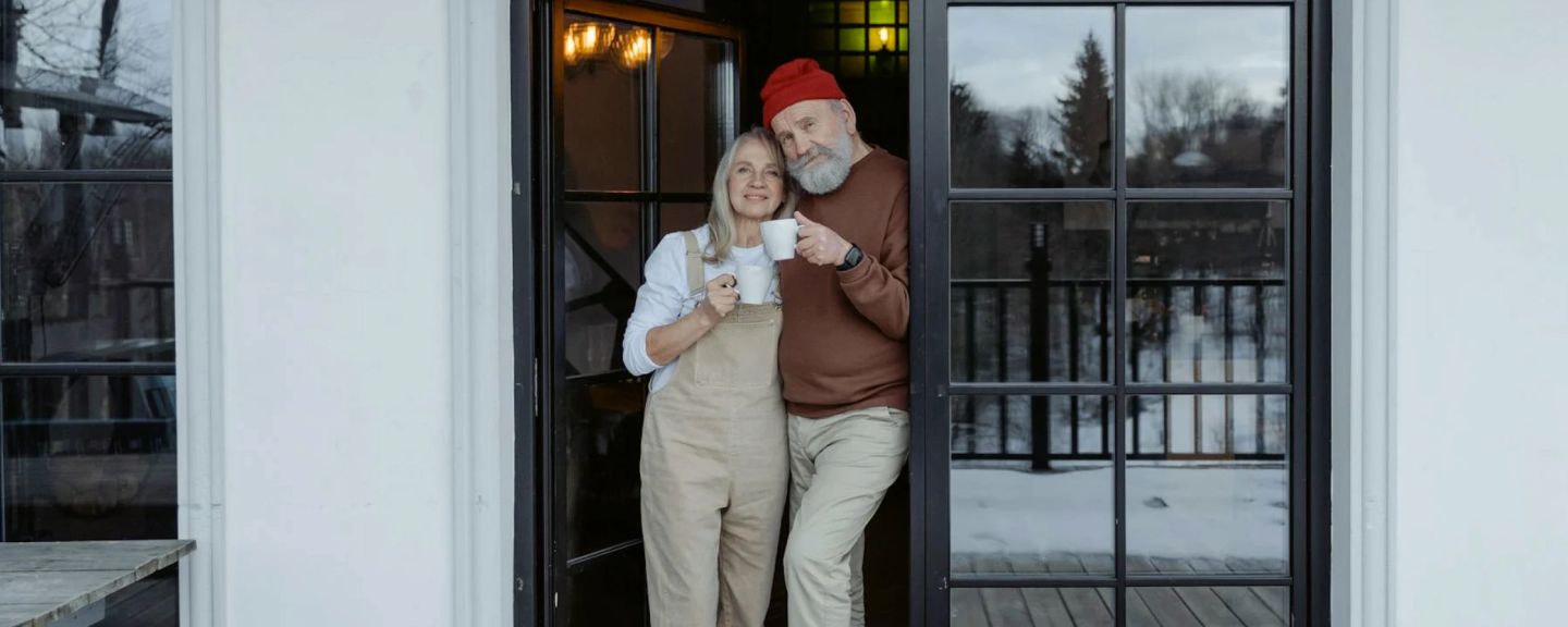 Two people standing in a doorway holding mugs, with snowy landscape visible behind them