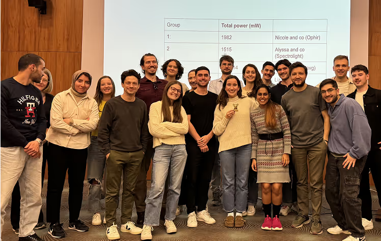 Group of approximately 20 people standing together in front of a presentation screen showing power measurement data
