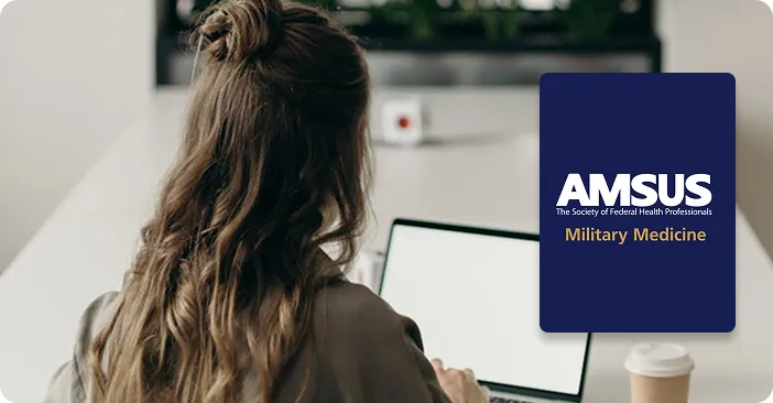 Person with long brown hair viewed from behind, sitting at a desk with a laptop and coffee cup, AMSUS Military Medicine logo displayed on right side