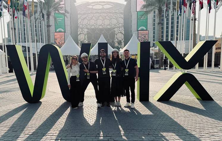 Team of five people wearing black outfits and lanyards standing between large yellow and black letters spelling "VIX" at an outdoor event venue