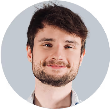 Man with dark hair and beard smiling at camera against light blue background