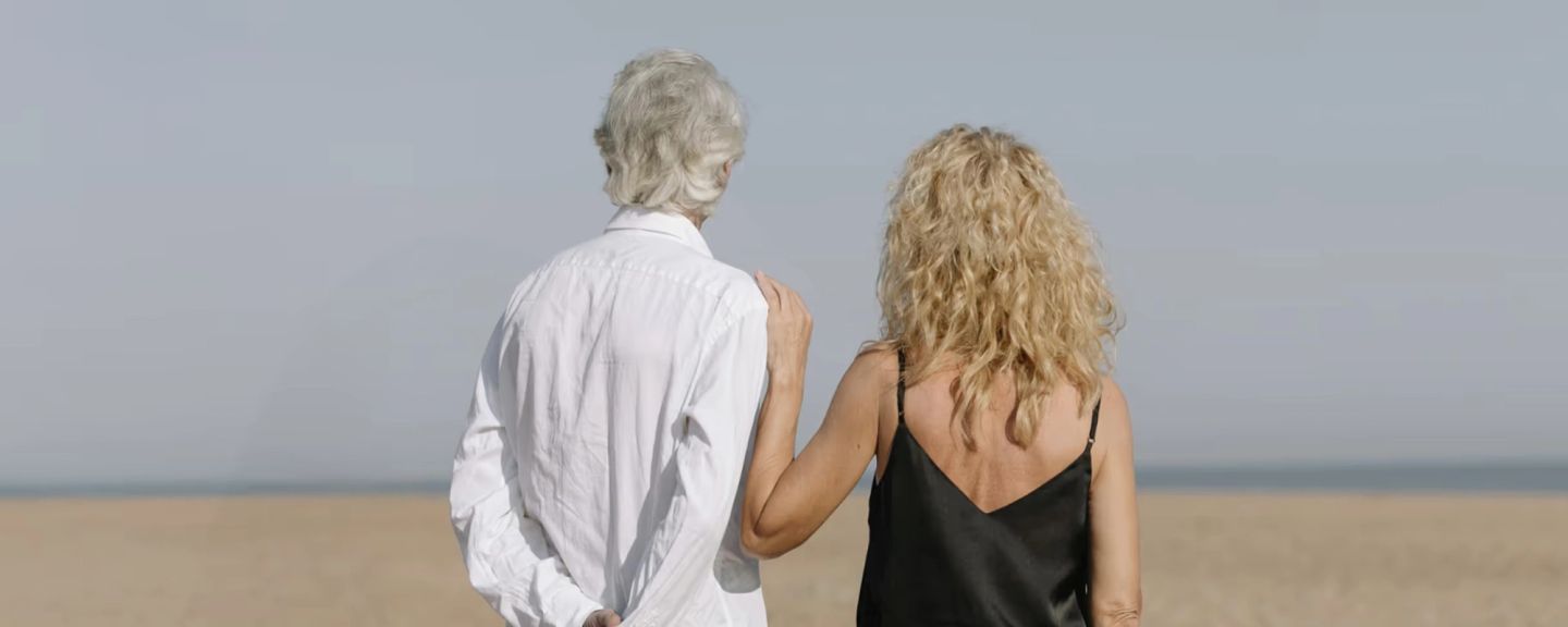 Two people standing on a beach facing the ocean, viewed from behind