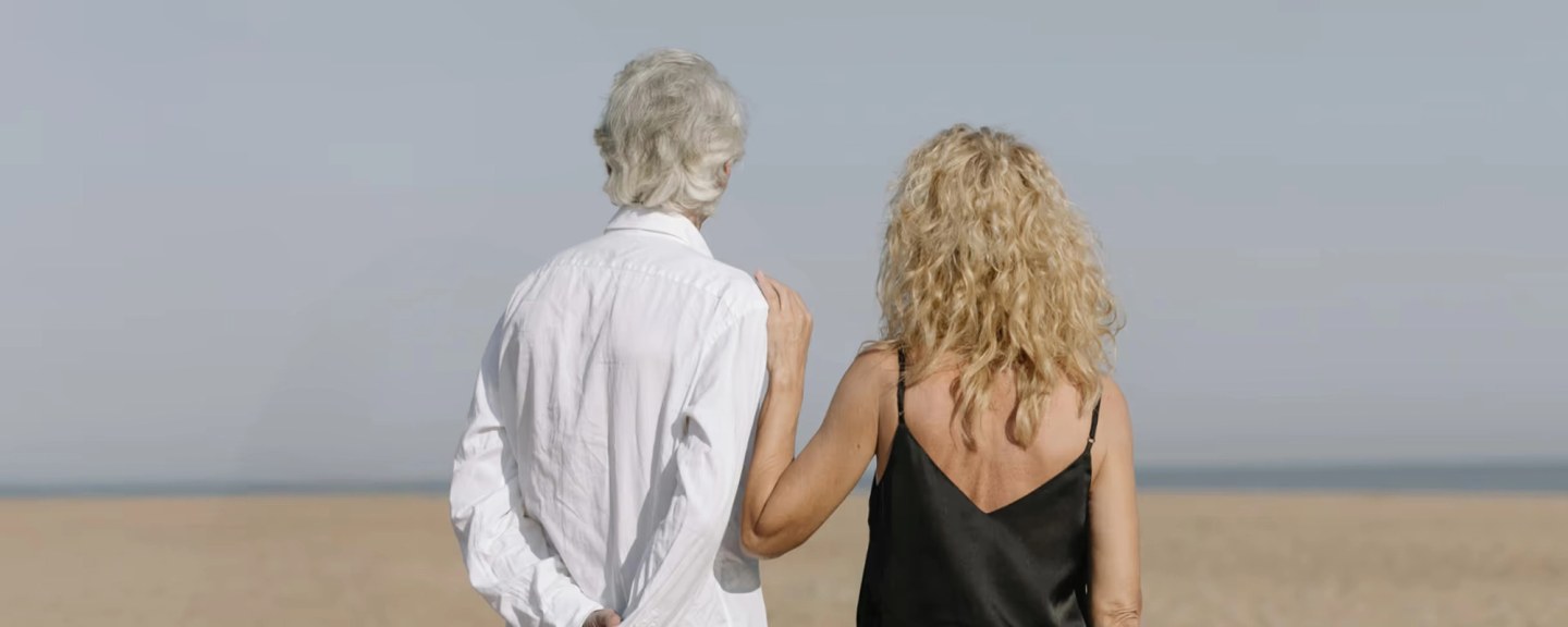 Two people standing on a beach facing the ocean, viewed from behind