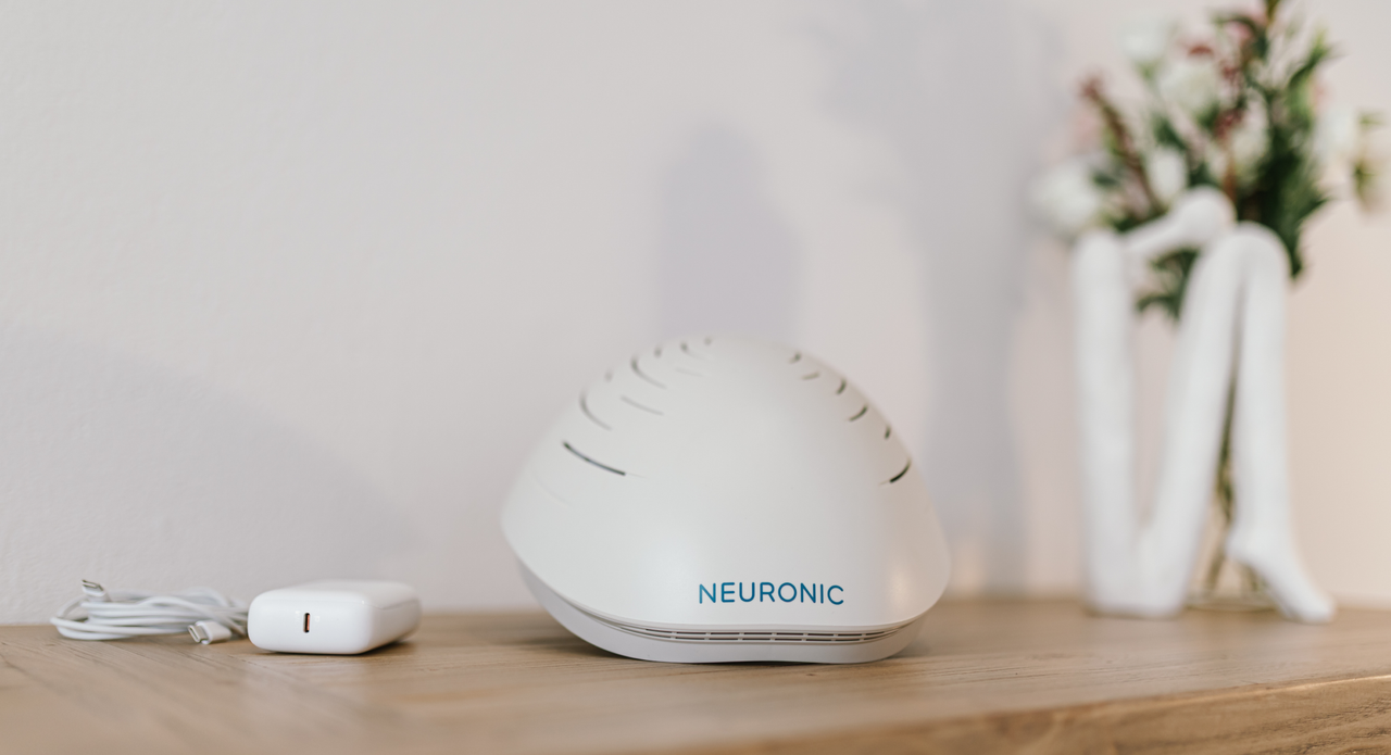 Neuronic Helmet in white, displayed on a wooden surface with control unit and power cable