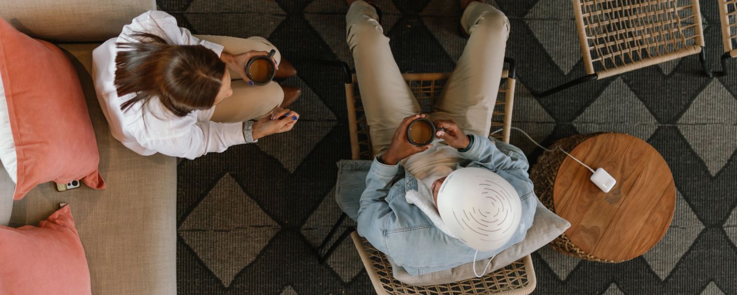 Overhead view of two people sitting on chairs holding mugs, with a wooden table and keyboard nearby