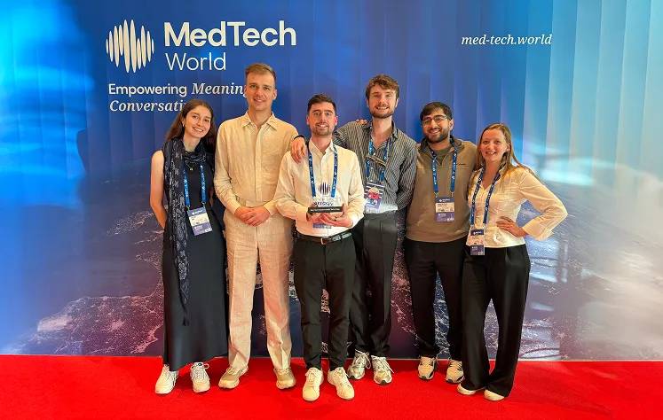 Six people standing together at MedTech World event, wearing conference badges, with branded backdrop behind them