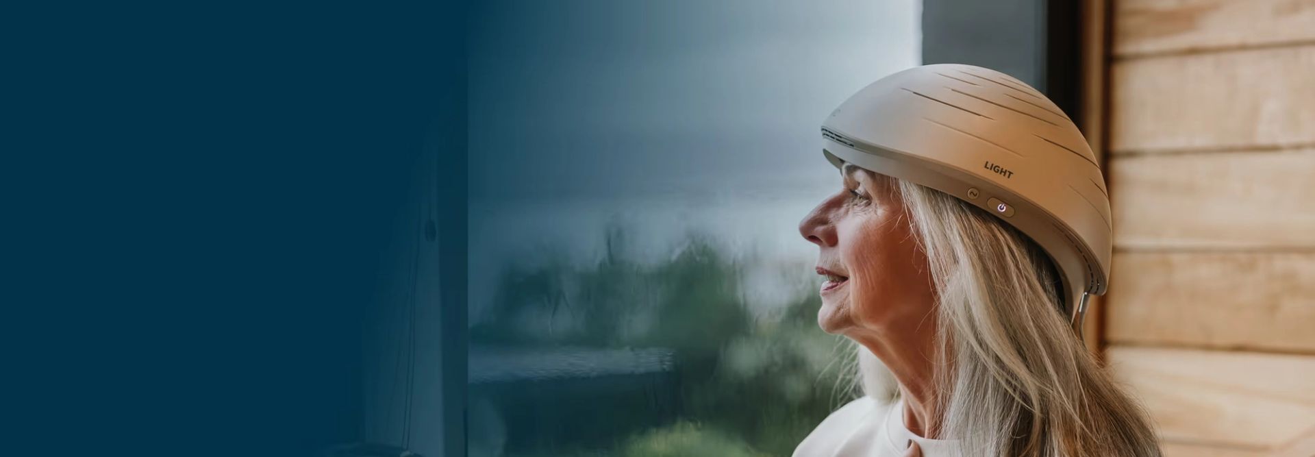 Woman wearing Neuronic LIGHT helmet, looking out window at forest landscape