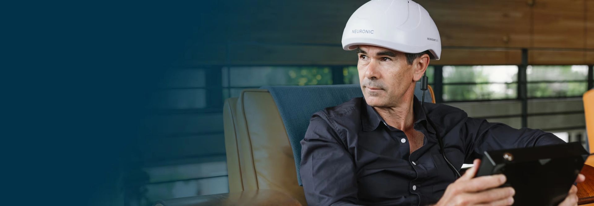 Man wearing white Neuronic Helmet seated indoors, holding a tablet device