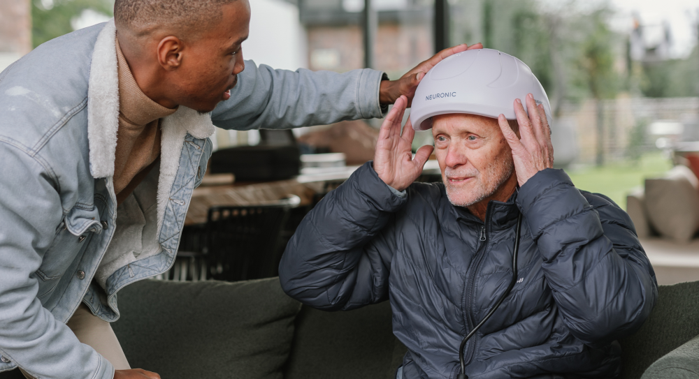 Man assisting an older man with fitting the Neuronic Helmet outdoors