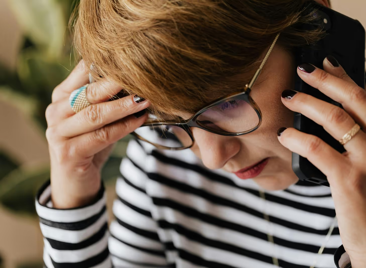 Woman adjusting eyeglasses, wearing striped shirt with manicured nails