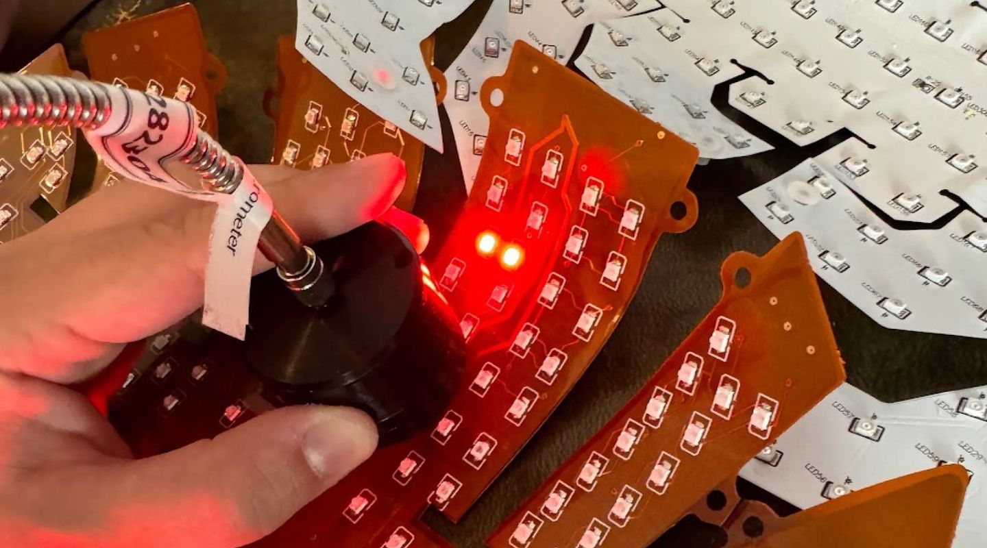 Hand holding Neuronic Helmet component with red LED lights illuminated on circuit board assembly