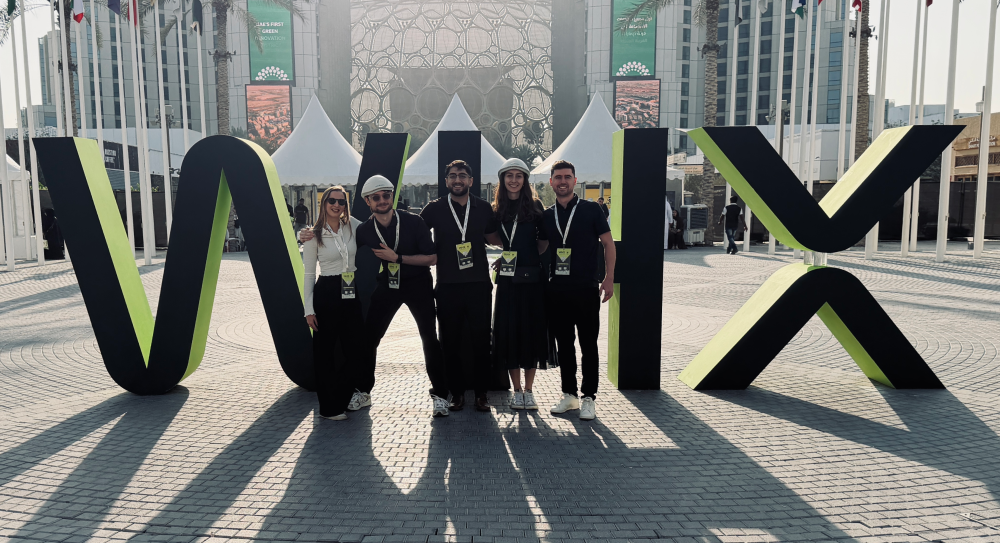 Five team members wearing lanyards standing between large geometric letters at an outdoor event venue