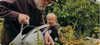 Three people examining a watering can outdoors in a garden setting