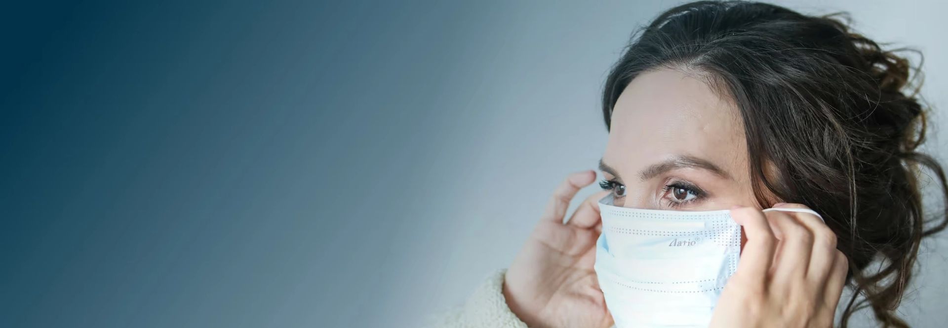 Woman with dark hair pulling a white medical mask up to her face