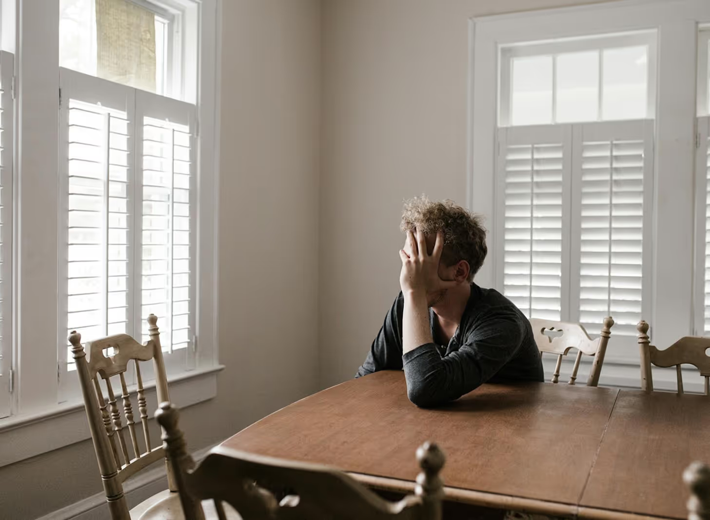 Person sitting at a table with head in hand, looking toward windows