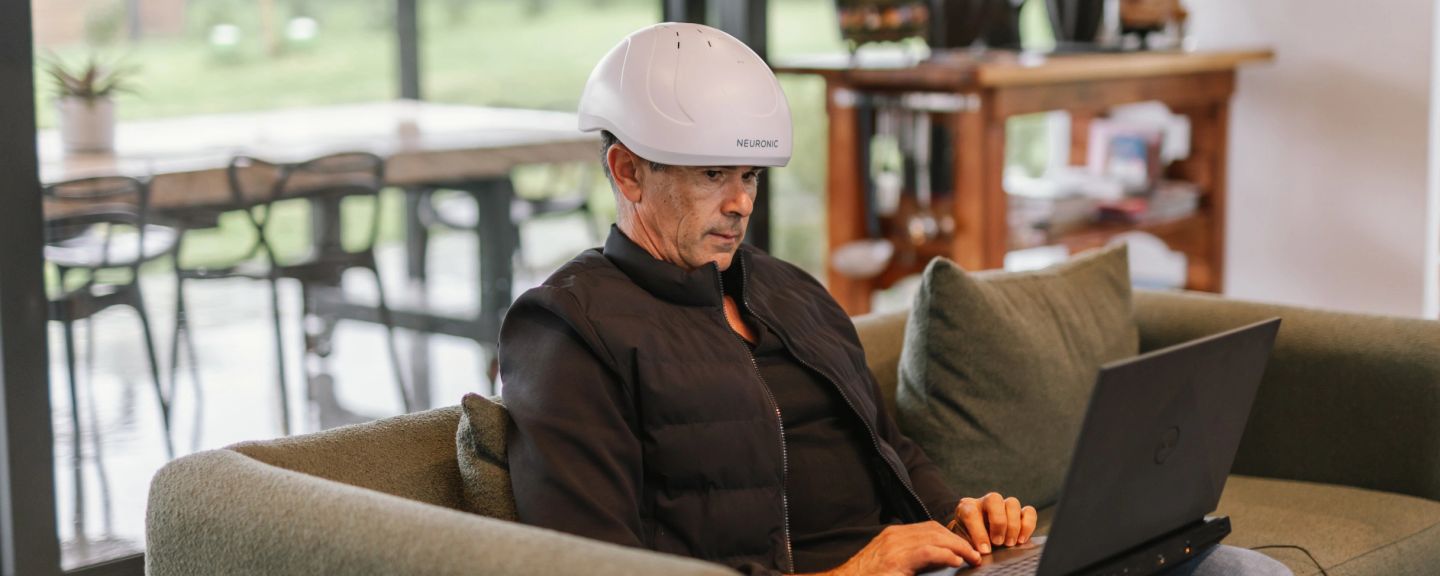 Man wearing Neuronic Helmet while using a laptop indoors