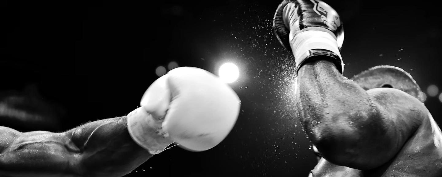 Two boxers' gloved hands colliding mid-punch against a black background, with impact spray visible