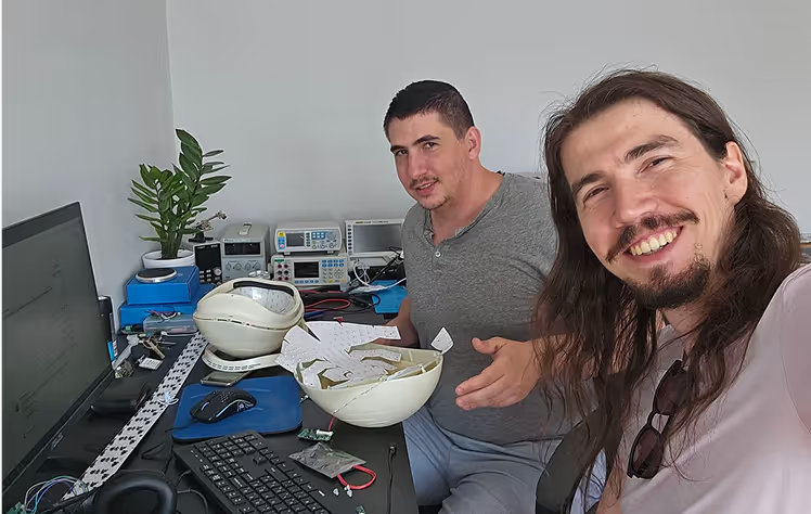 Two men in a laboratory setting with computer equipment and instruments, smiling at camera