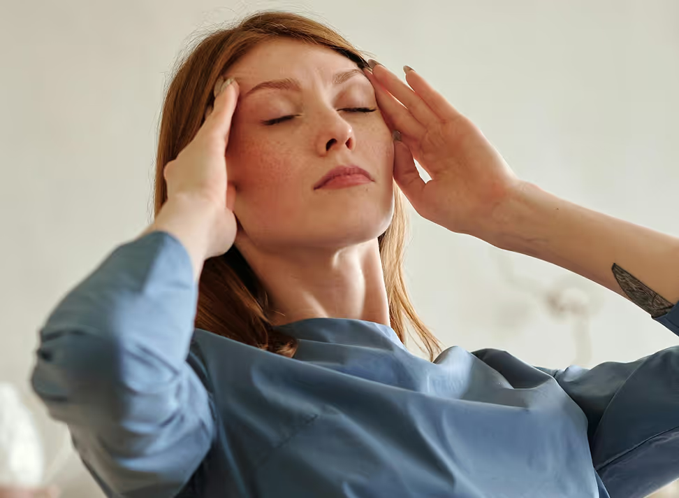 Woman with eyes closed, hands on head, appearing to experience discomfort or tension