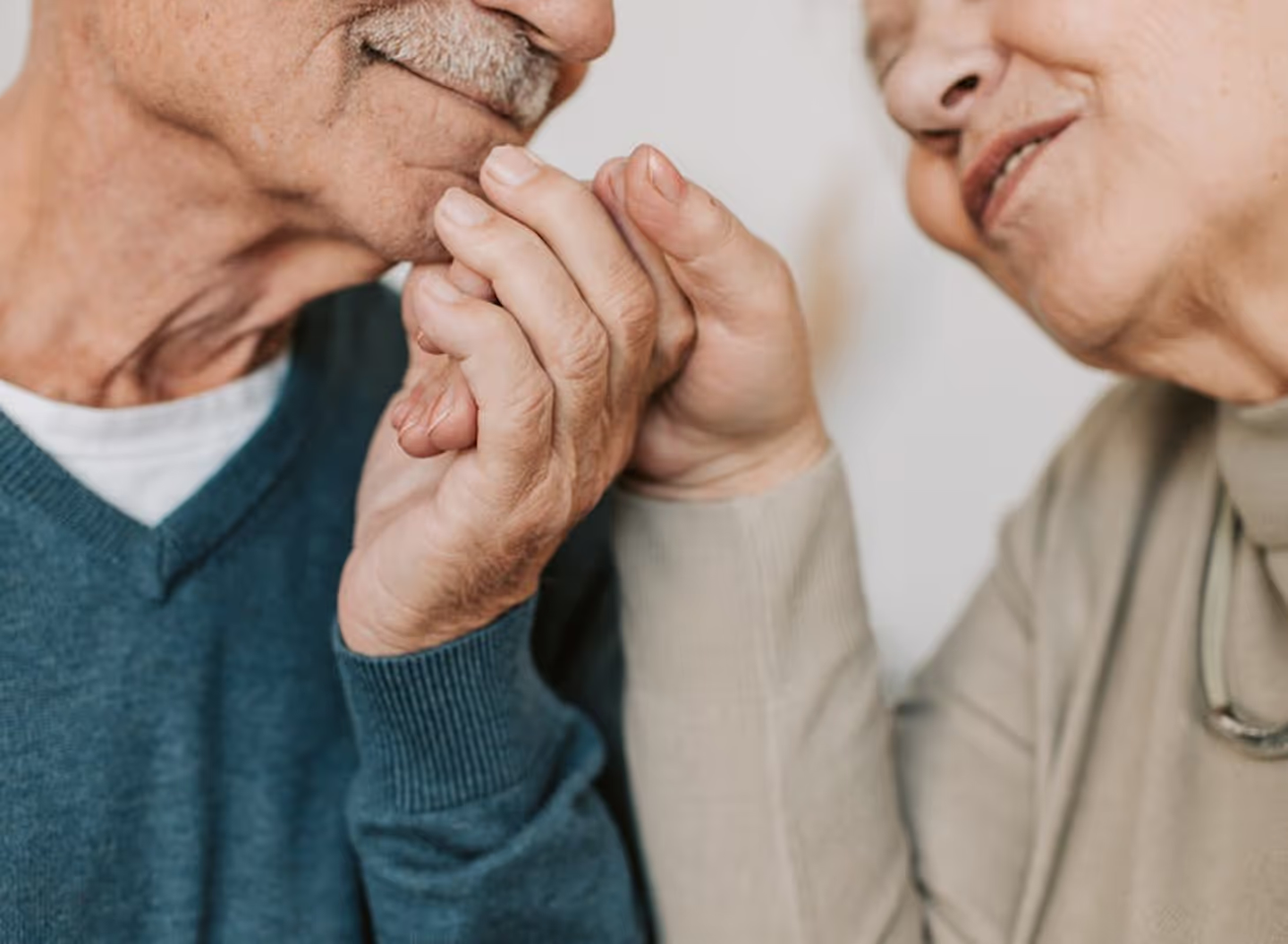 Two people holding hands, man on left wearing blue sweater and woman on right wearing beige sweater