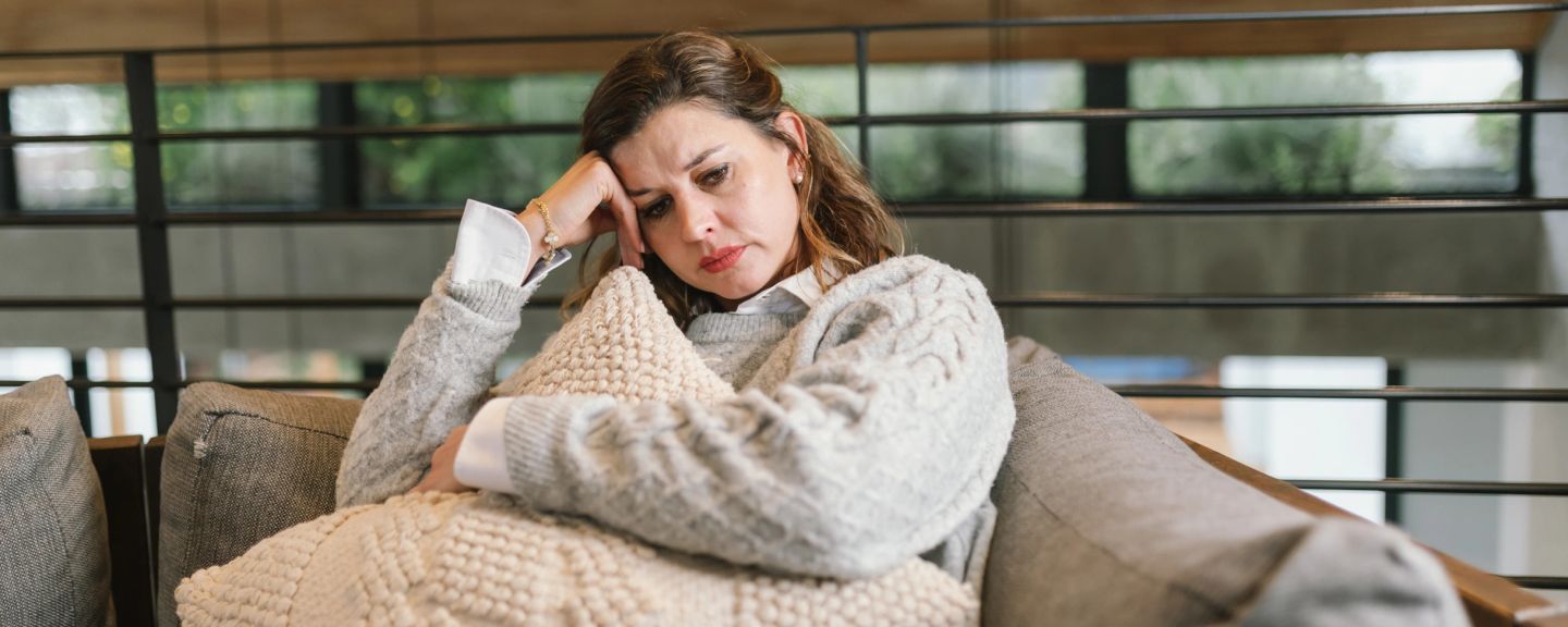Woman sitting on couch with hand to face, looking downward with concerned expression