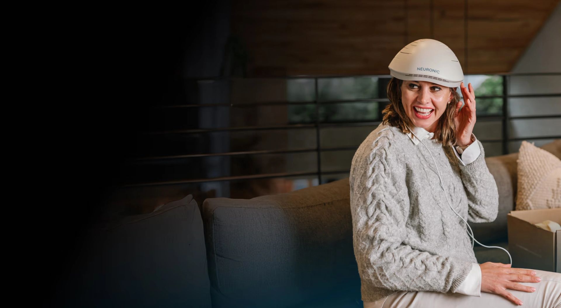 Woman wearing the Neuronic Helmet, smiling at camera while seated on a couch