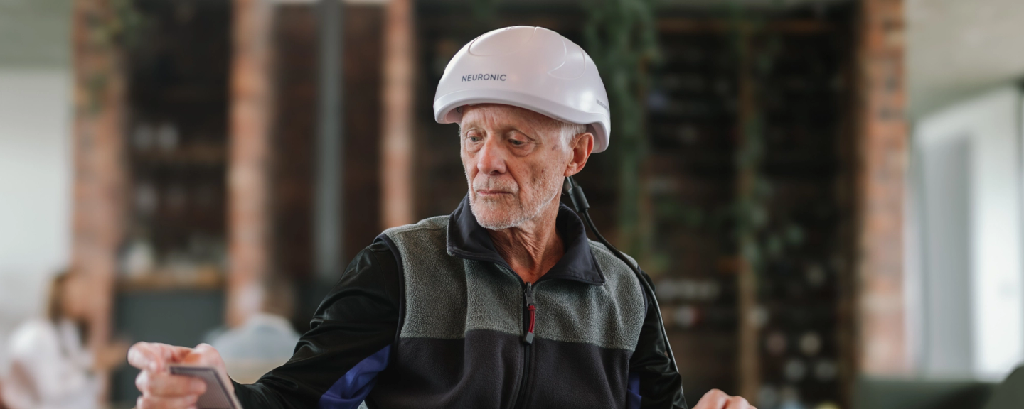 Older man wearing Neuronic Helmet, eyes closed, outdoors in casual clothing