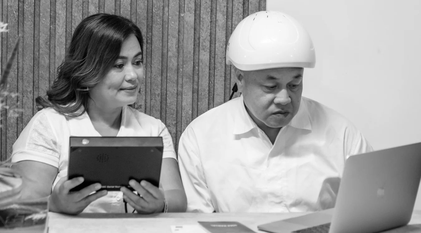 Man wearing Neuronic Helmet working at laptop with woman holding tablet beside him