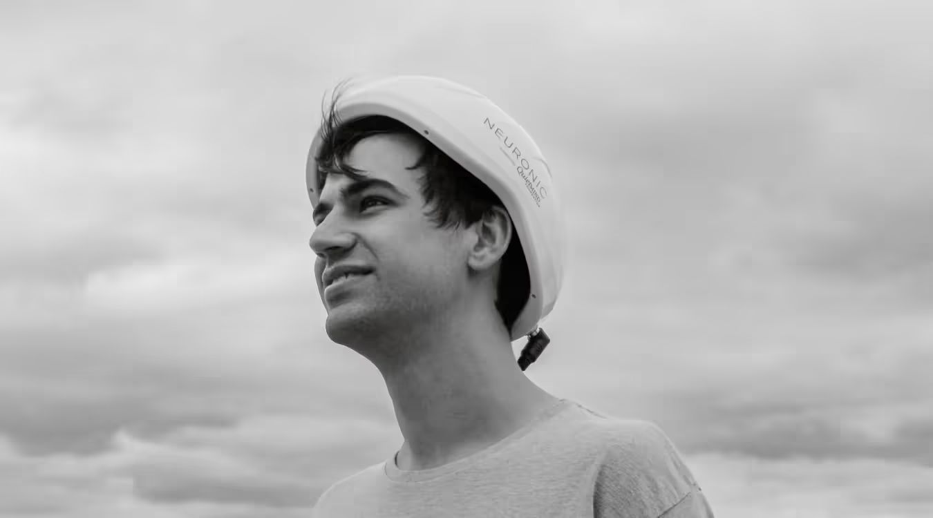 Man wearing Neuronic Helmet with chin strap, looking upward in profile against cloudy sky