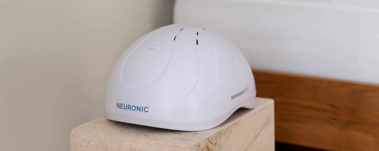 White Neuronic Helmet with dome design and curved panel lines, displayed on a light stone surface
