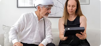 Older man wearing white shirt and cap looking at tablet held by woman in black sleeveless top