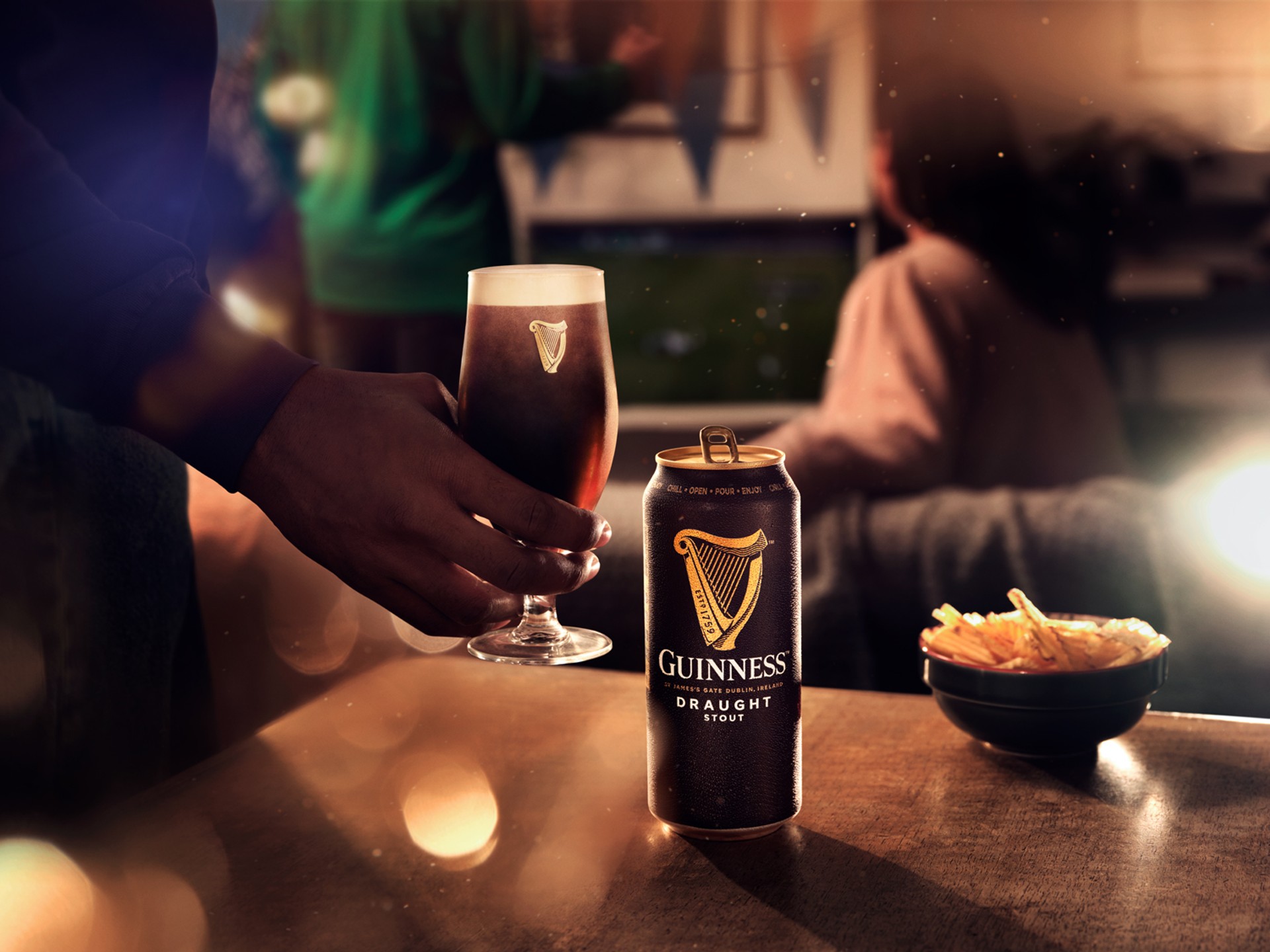 Hand holding a pint of Guinness in a living room with a group of friends photographed by Jason Bailey Studio.