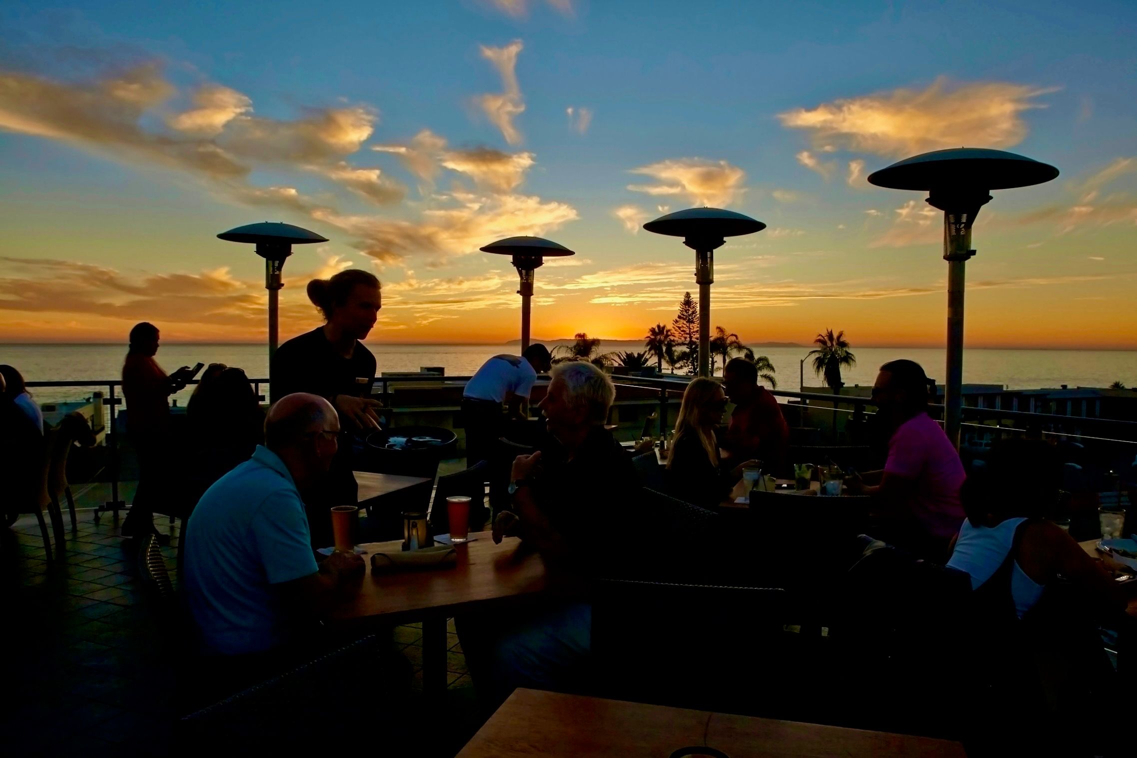 Guests dining and toasting at sunset on the ocean-view rooftop