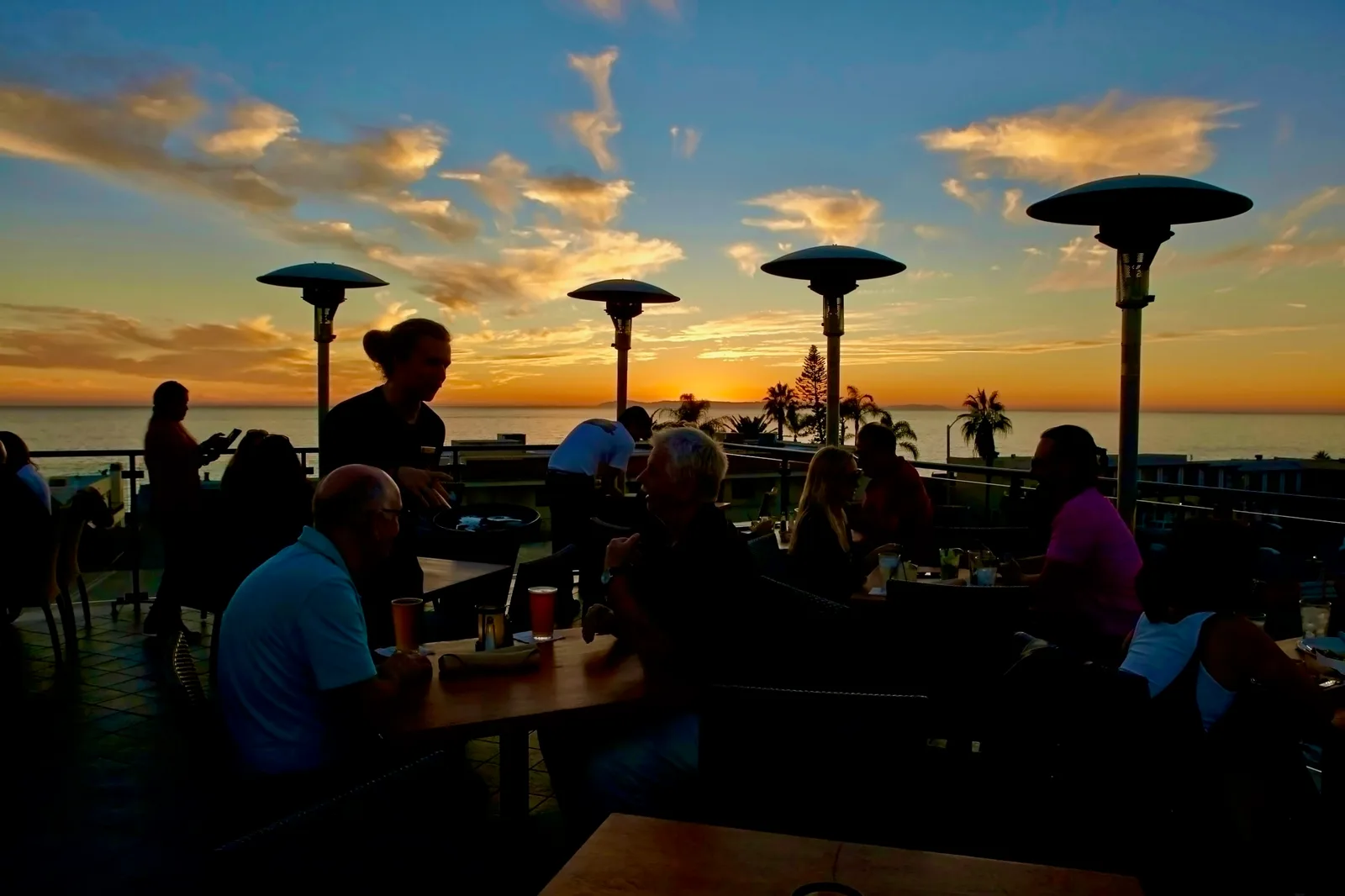 Guests dining and toasting at sunset on the ocean-view rooftop