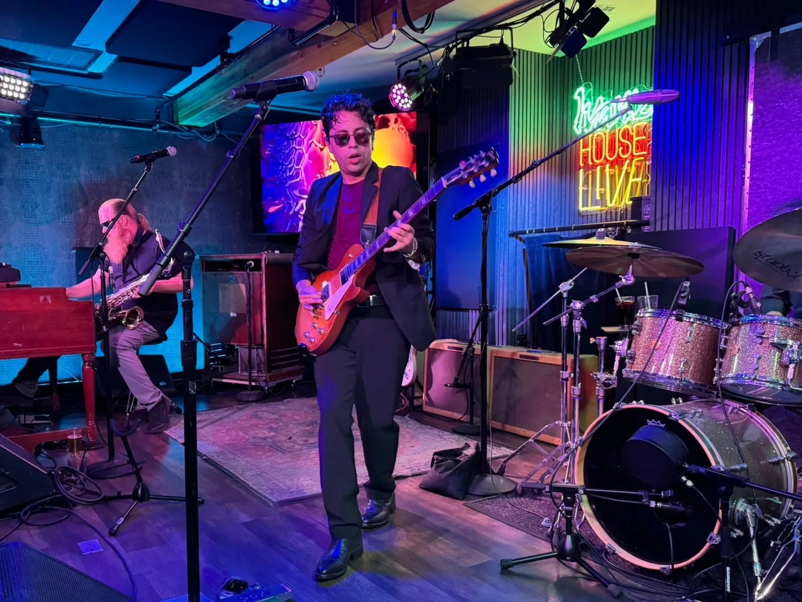 Guitarist and band performing in front of the Ivan'z House Live neon sign