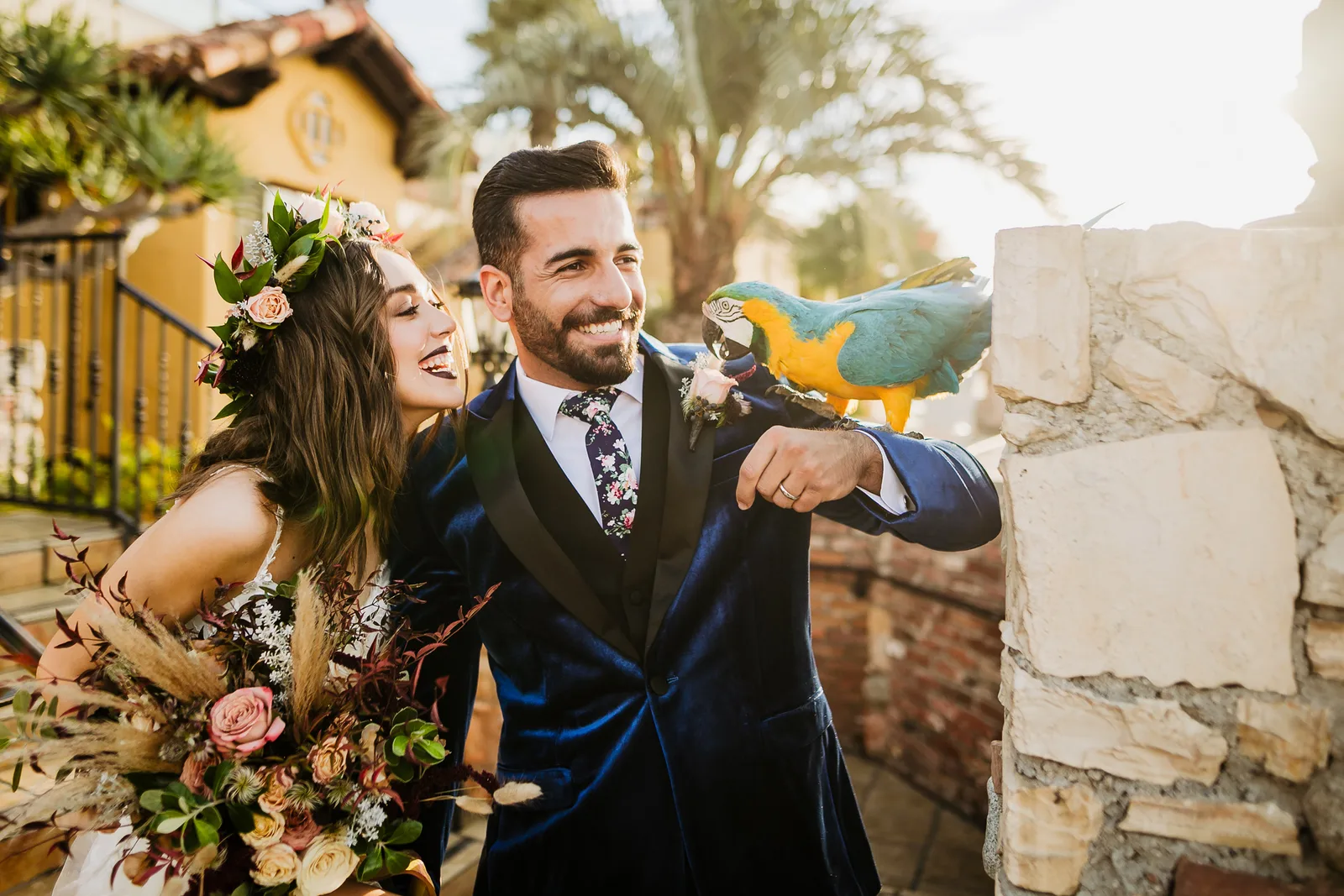 Wedding couple beside a scarlet macaw perched on a stone wall at the venue archway