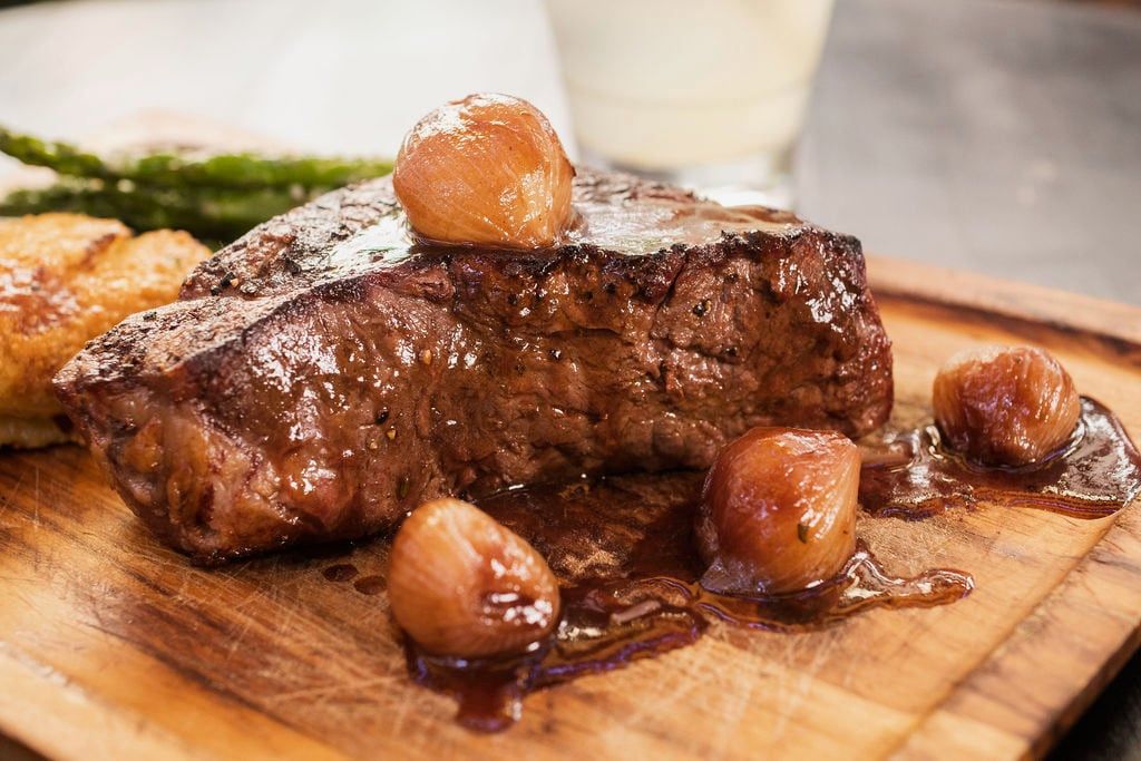 New York strip with cipollini onions on a wooden board