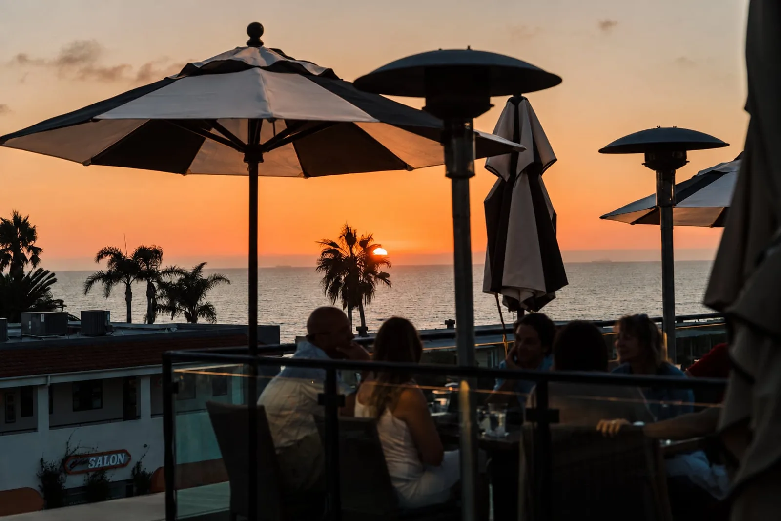 Diners under umbrellas on the rooftop at sunset over the ocean
