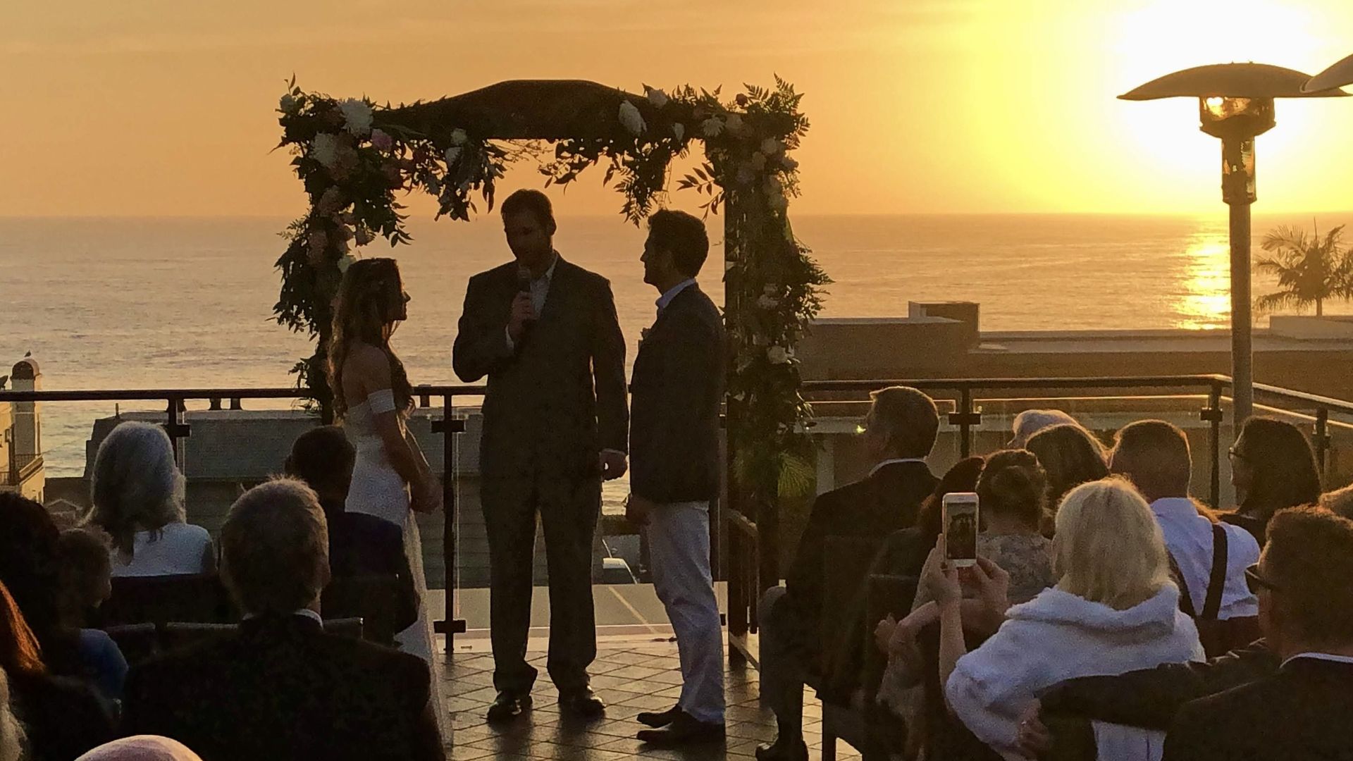 Couple exchanging vows under a floral arch on the Veranda Rooftop at sunset