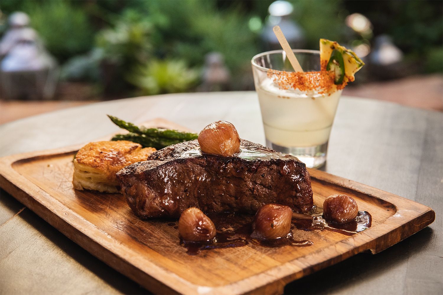 Plated steak with roasted potato, asparagus and a cocktail on a wood board