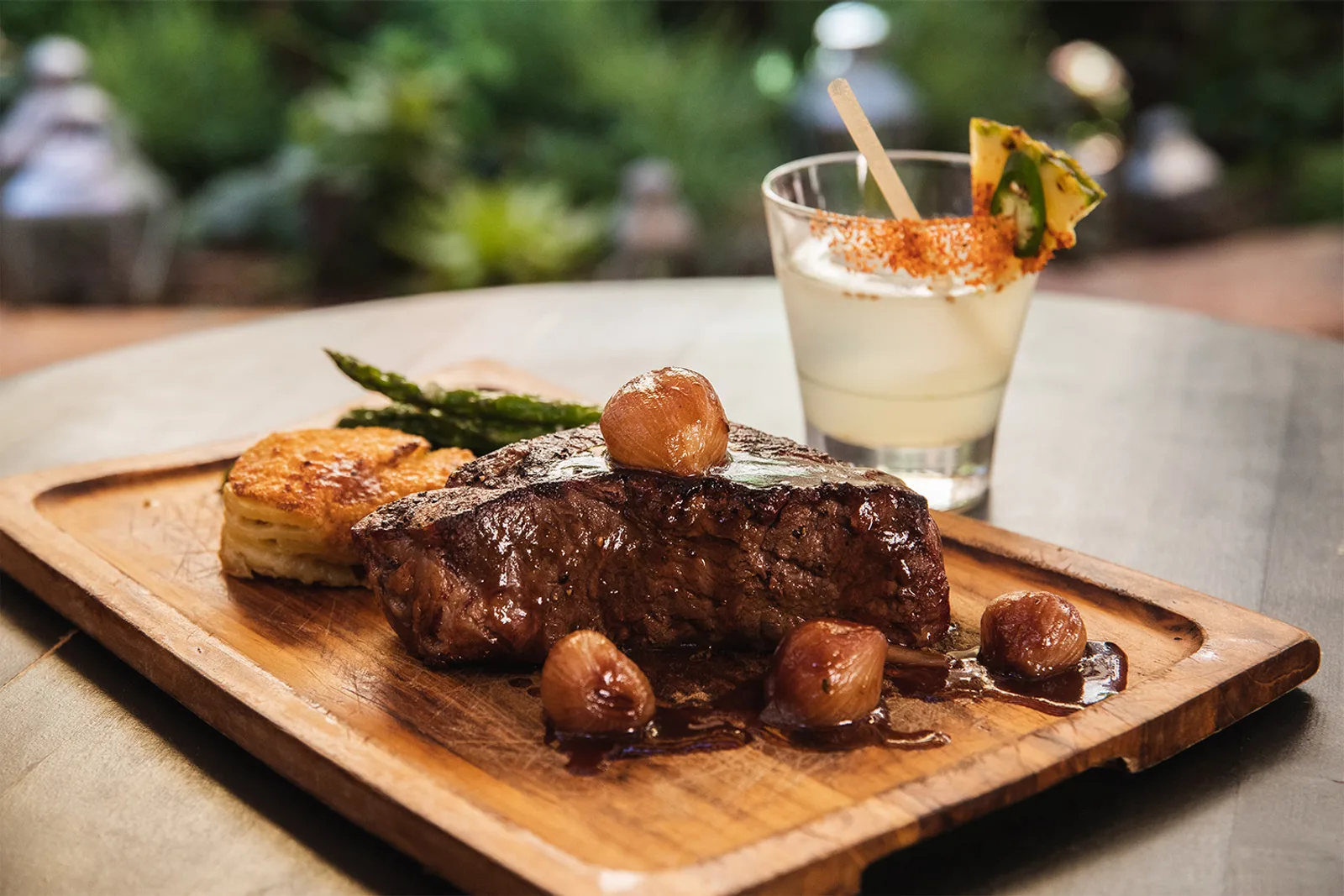 Plated steak with roasted potato, asparagus and a cocktail on a wood board