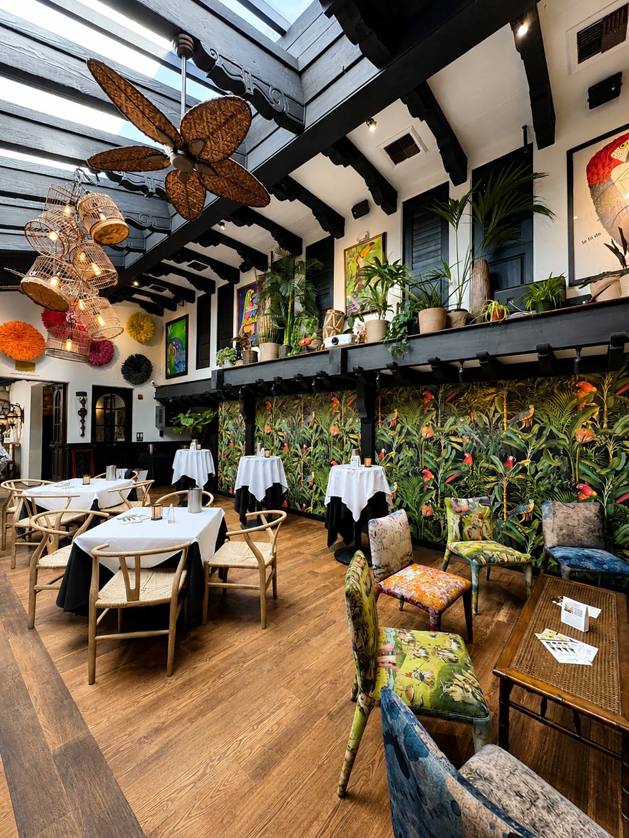 Parrot Room set with white-linen tables beneath a skylight and tropical mural