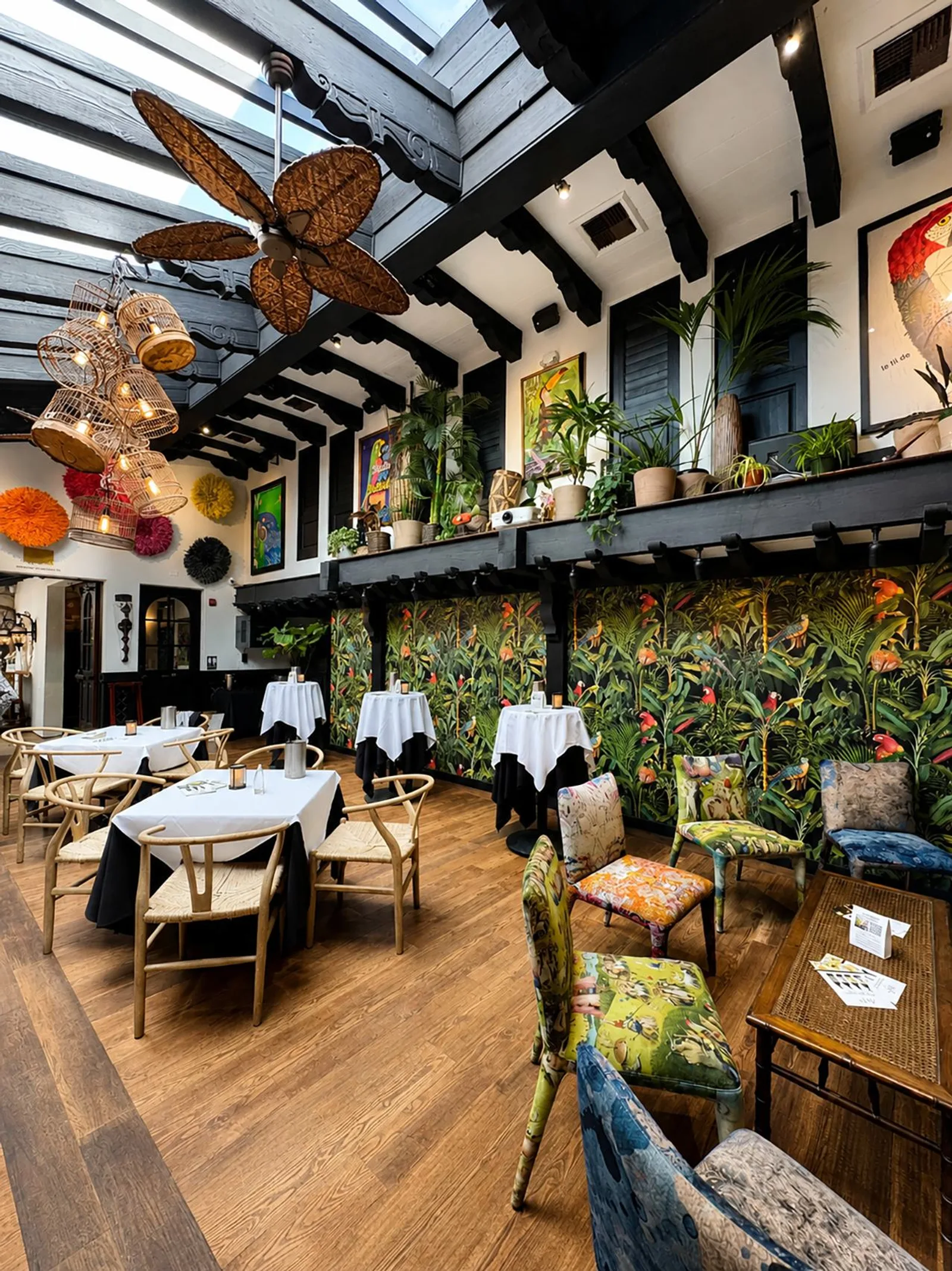 Parrot Room set with white-linen tables beneath a skylight and tropical mural