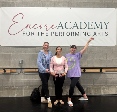 Adults pose together in front of an Encore Academy sign