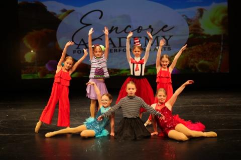Performers pose together on stage in colorful costumes