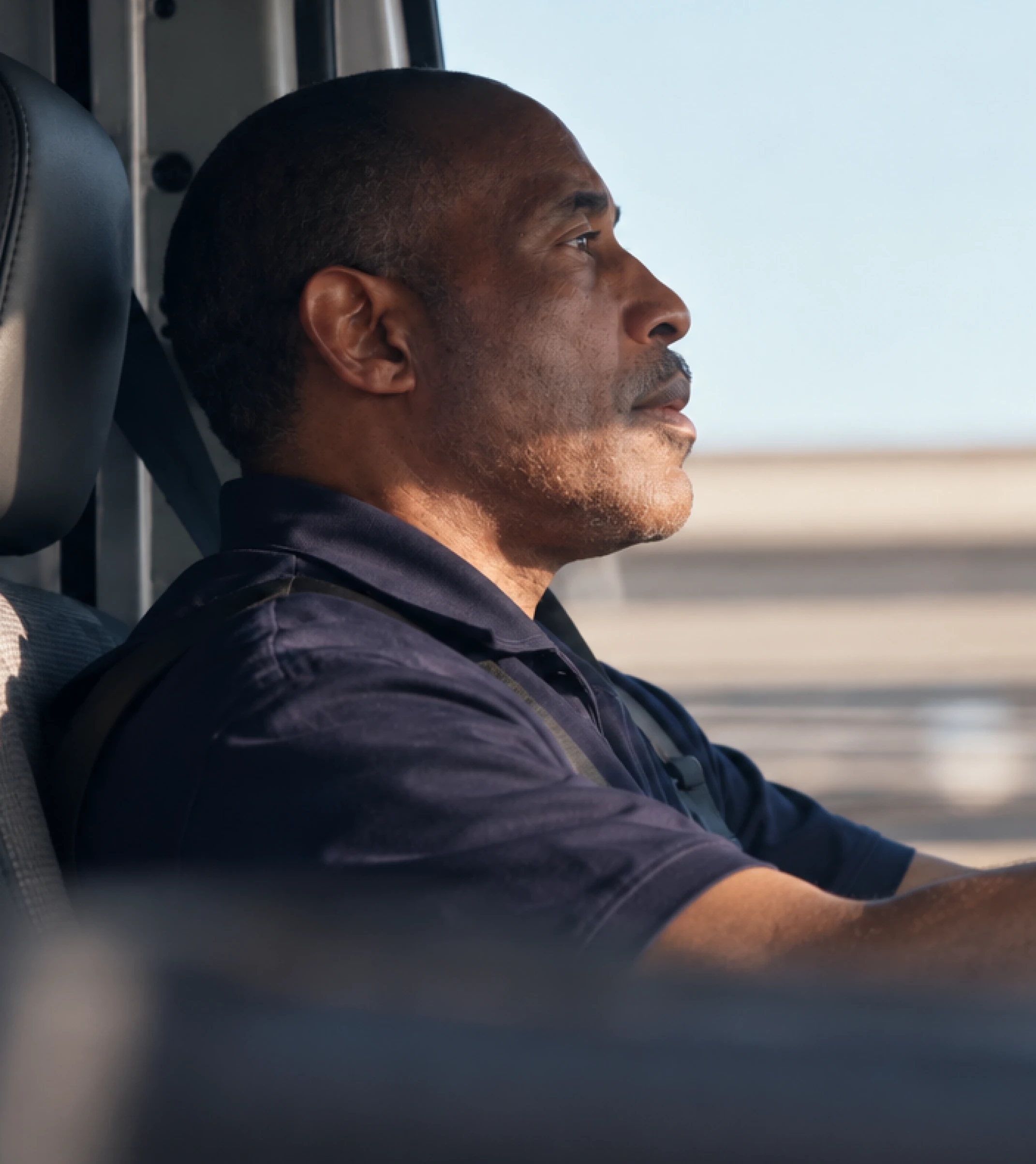 A driver in a navy polo shirt at the wheel, looking out at the road