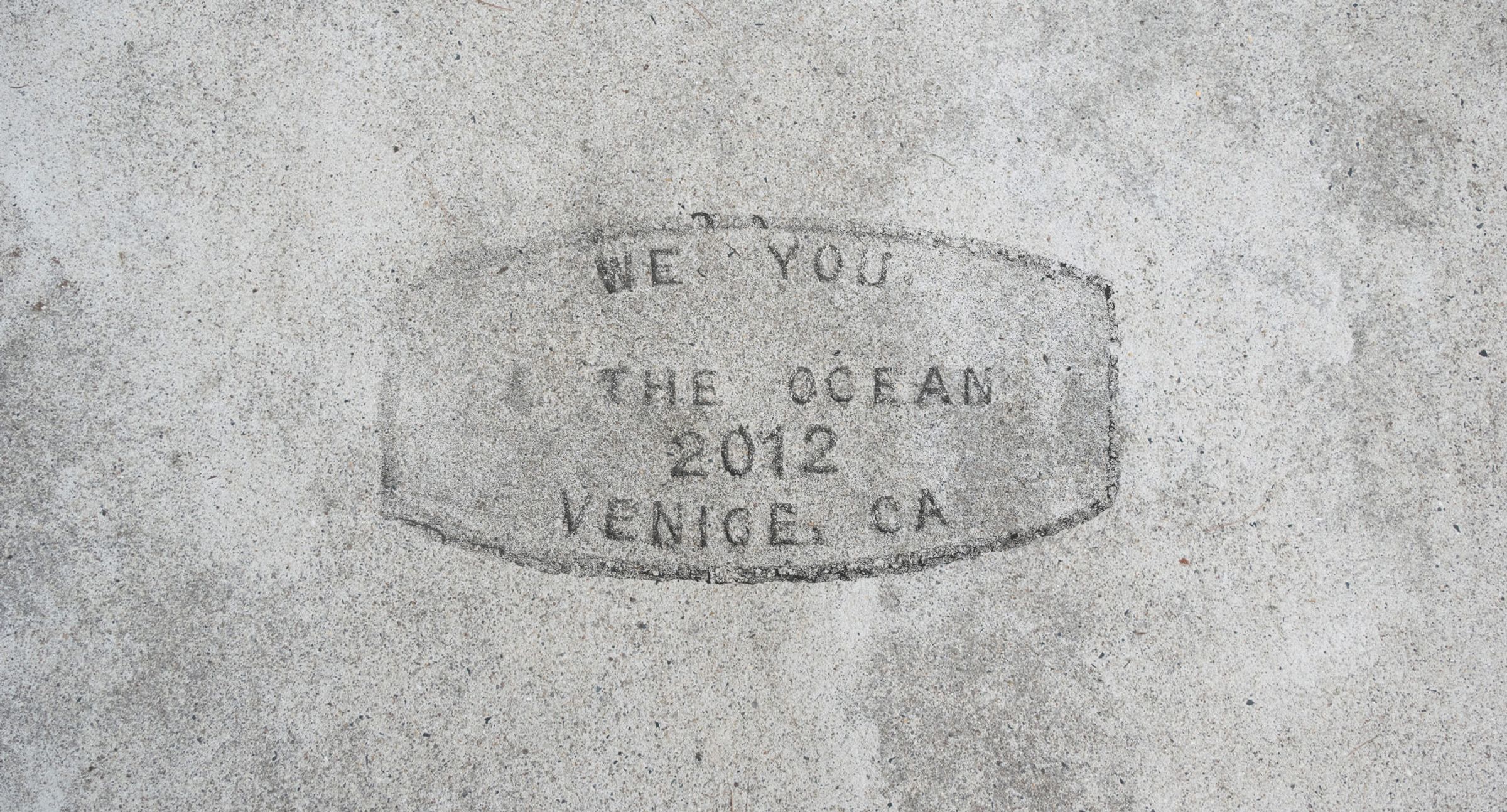 Concrete sidewalk stamp reading 'We love you the ocean, 2012, Venice CA'