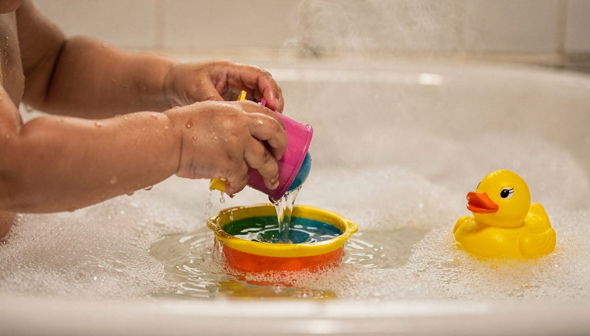 Toddler's hands playing with water and foam in the bathtub, sensory play during children's bath time
