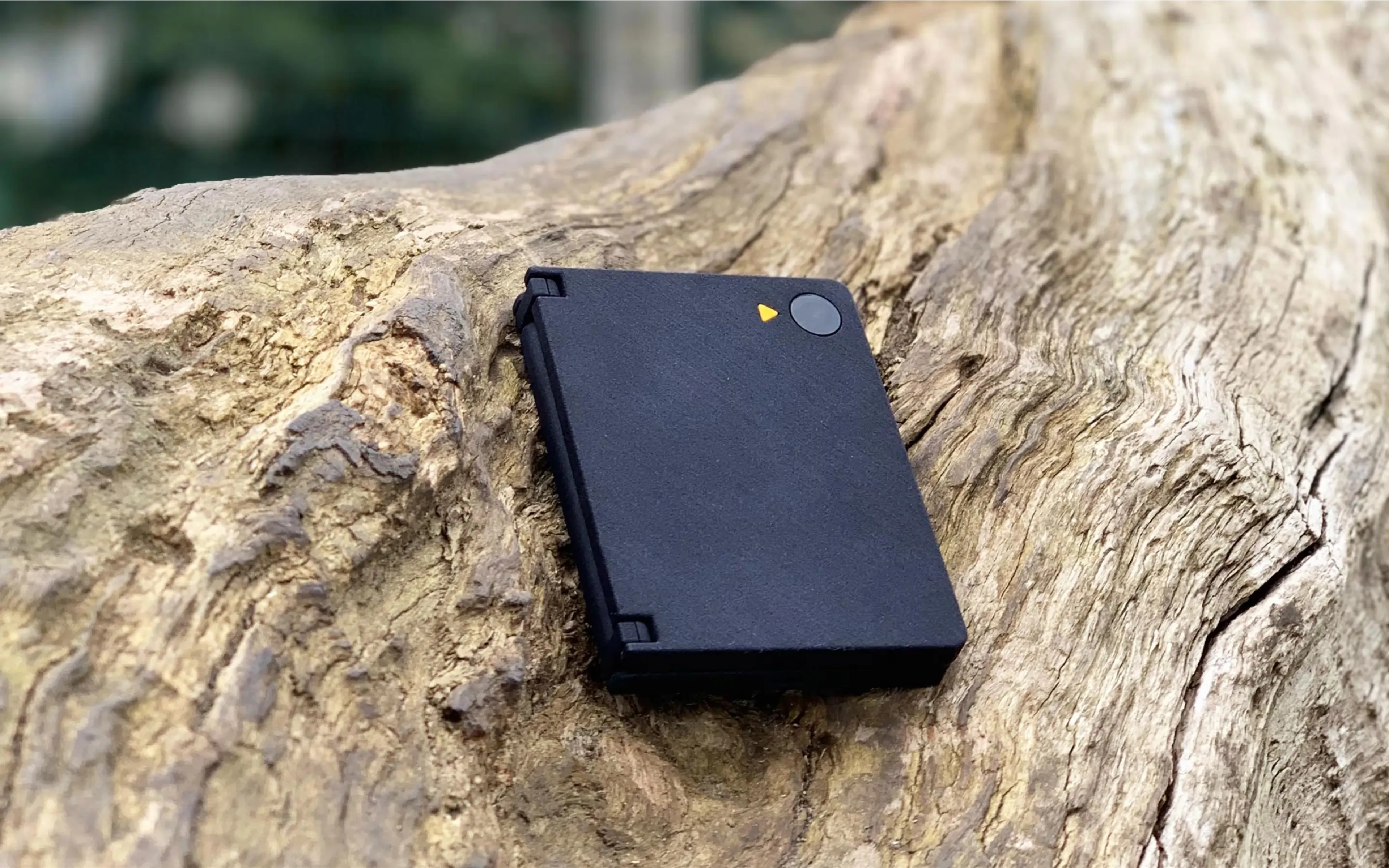 Ash AI Pokedex device closed, resting on a log