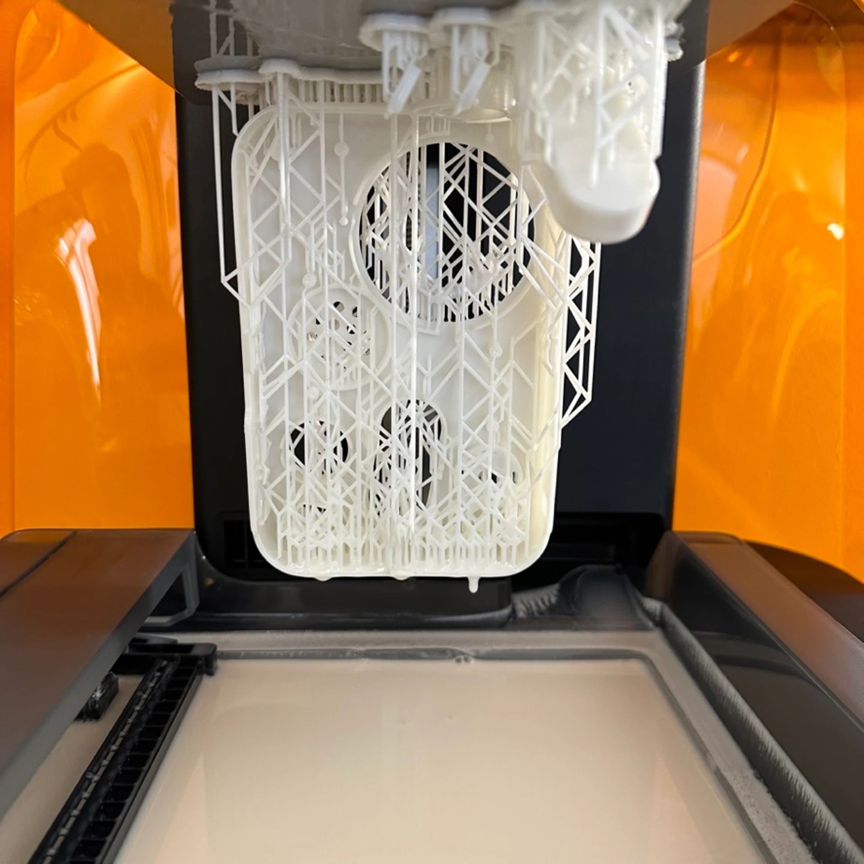 A resin part curing on the printer, still hanging from its support lattice